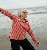 Elderly women stretching on the beach near water.