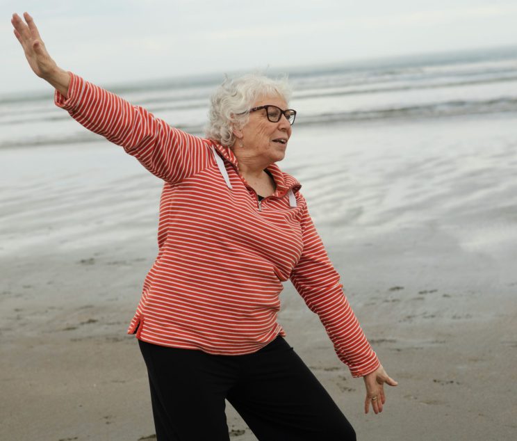 Elderly women stretching on the beach near water.